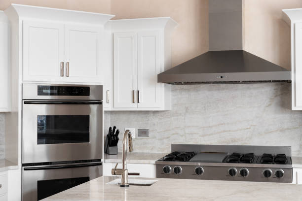 A kitchen detail with white cabinets, white marble countertop and backsplash, stainless steel appliances, and a polished nickel faucet.
